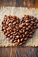 Sack of coffee beans is torn and the heart-shaped piece of cloth holding the beans is visible. - obrazy, fototapety, plakaty