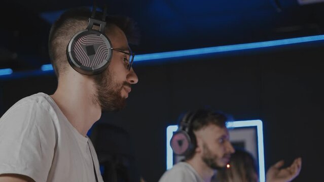 Happy smiling bristly adult gamer in headset playing PC video game at computer club with team cyber sport tournament. E-sport championship. Multiplayer online real-time strategy first-person shooter