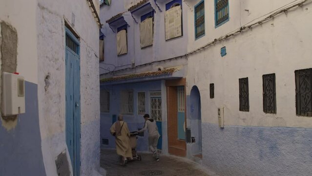 Couple running with baby stroller on empty street of blue city of Chefchaouen