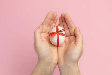 Easter egg with a red ribbon in female hands.