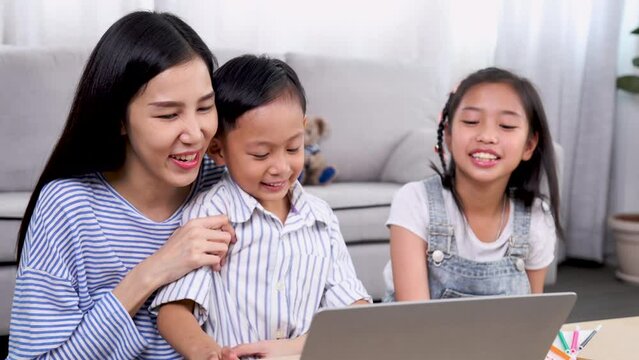 Asian mother or teacher using laptop computer teach homework for primary school children or private tutoring, boy and girl siblings watching cartoons together, family relationship mom with kids