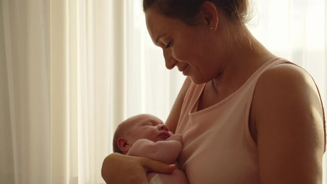 A happy mother holds and kisses baby in her arms, silhouette. A cute infant sleeps in his mother's arms. Concept of happy parenthood. Mother is rocking her newborn son in her arms. Mother and child.