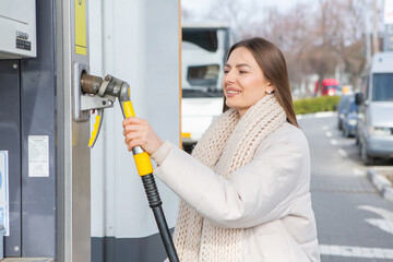 Young woman refueling car with gasoline at gas station. Eco fuel concept. The concept of...