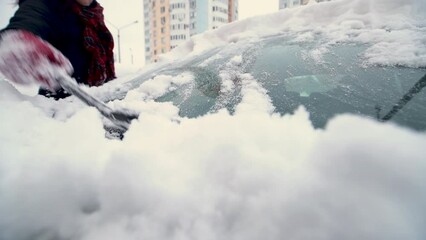 Close-up of a woman removing snow from the windshield of her car after a heavy snowfall. Concept of winter weather, car maintenance and preparation for snowy conditions