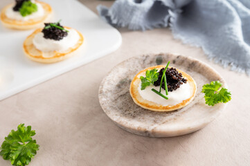 Mini pancake or blinis with sturgeon black caviar on marble plate.