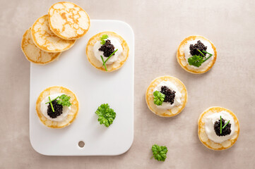 Appetizer, black caviar with pancake and sour cream on white plate.