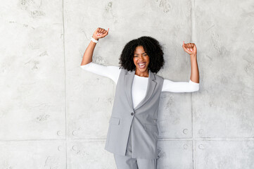 An exuberant African-American businesswoman celebrates with her arms raised against a textured gray...