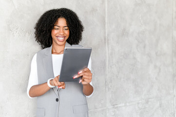 Cheerful African American businesswoman holds a digital tablet, her smile reflecting success and digital proficiency. A modern, tech-savvy professional in a casual corporate setting.
