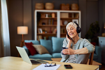 A relaxed senior adult female freelancer listening to music and drinking coffee while taking a small break from work - Powered by Adobe