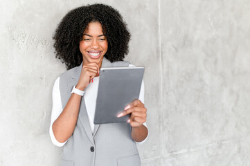 A young African-American businesswoman with an infectious grin uses a tablet, showcasing a balance...