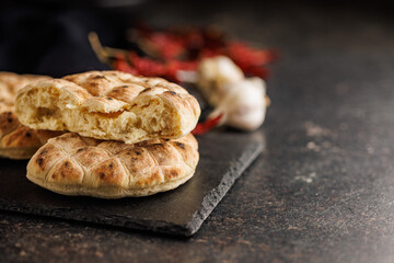 Arabic flat pita bread on cutting board on black table.