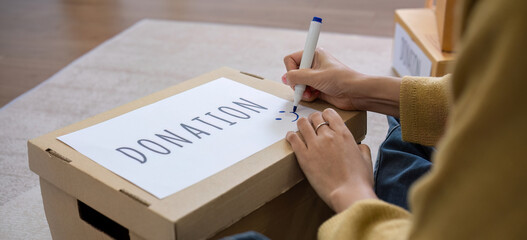 A beautiful Asian woman uses a magic marker to write on a box of clothes that will be donated to...