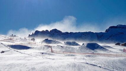 Snowpark and skislope in Italy (Alpe di Siusi in Val Gardena) on top of the mountains, during a heavy wind storm, causing a snowstorm and beautiful sights underneath a clear blue sky in de Dolomites. 