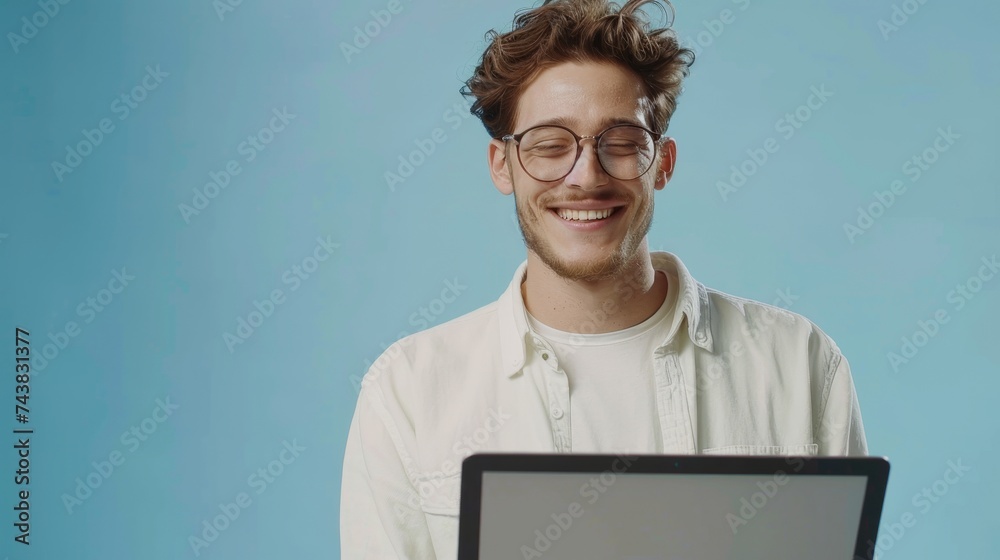 Poster Millennial in glasses working online or communicating on laptop computer in blue studio background