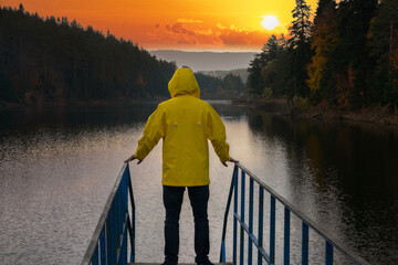 Man standing on the bridge over the lake in a yellow raincoat. Sunset view at Bozcaarmut lake.