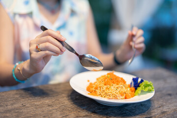 Side view of a foodie using a spoon to eat noodles. There are vegetables and noodles. Beside it, a...