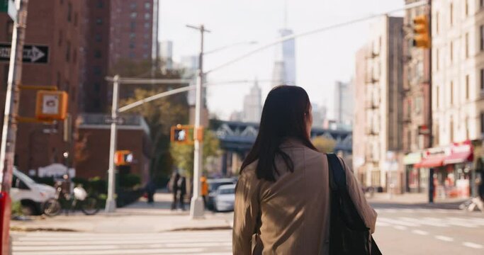 Camera follows young local brunette female walking in urban streets of New York City on sunny day.
