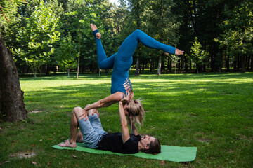 Boy and girl doing acro yoga outdoors in summer in public park