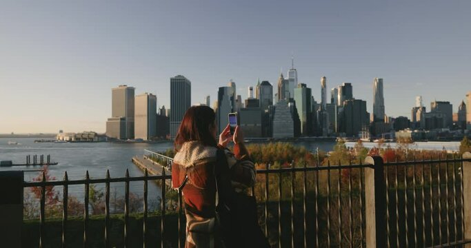Attractive young female taking pictures and videos of iconic Manhattan skyscrapers using phone