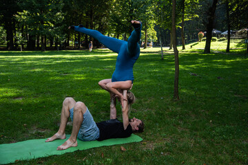 Boy and girl doing acro yoga outdoors in summer in public park
