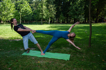 Boy and girl doing acro yoga outdoors in summer in public park