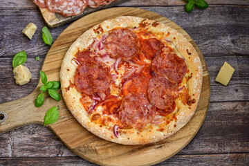Home made italian  pepperoni   pizza with  tomatoes, mozzarella and parmesan cheese and fresh basil  on wooden background