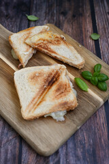 Toasted sandwich with  ham, cheese and basil  served on wooden cutting board