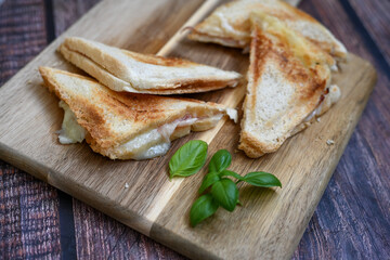 Toasted sandwich with  ham, cheese and basil  served on wooden cutting board