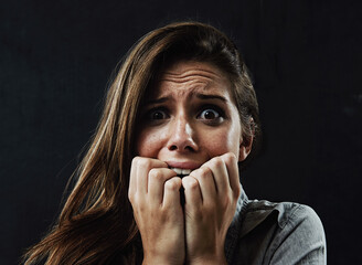 Portrait, mental health and woman biting nails in studio on black background for reaction to fear or panic. Face, stress and horror with scared young person in dark for drama, nightmare or terror