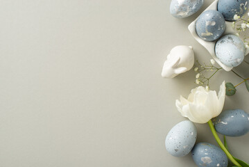 Easter composition: Overhead perspective of charcoal grey eggs in a bespoke ceramic pot, bunny effigy, gypsophila, tulip, and eucalyptus arranged on a pastel grey background, including space for copy
