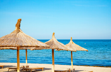 Sun canopies with a thatched roof on the beach near the sea.