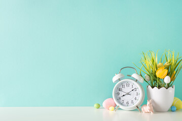 Easter tabletop arrangement: A side view of a setting with a shell-shaped flowerpot, tulips, grass, a ceramic bunny, eggs, and an alarm clock, against a light turquoise wall background