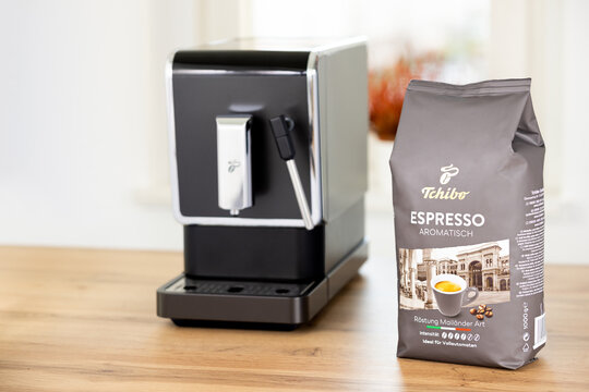 German Tchibo whole grain 1 kg pack in aromatic espresso flavor in a studio shot next to a Tchibo coffee maker machine.
