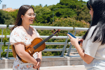 young latina busker violinist woman giving her phone number to tourist outdoors.