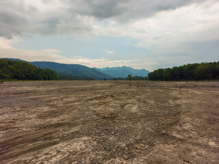 Vast dry river bed surrounded by green forest, blue mountain amid beautiful Cloudscape. The overcast monsoon weather and vast open landscape are the best places for adventure-seeking tourists.