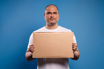 Portrait of a Brazilian man wearing a basic white shirt, from the front, holding a cardboard sign with both hands, serious and looking at the camera - Belém - Pará - Brazil - obrazy, fototapety, plakaty