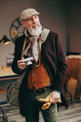 Portrait d'un photographe créatif et original  de type hipster très élégant et stylé avec un manteau un béret et un gilet dans un atelier créatif