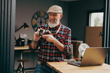 Portrait d'un homme photographe hipster dans un studio atelier et qui tient un appareil photo vintage en souriant devant un ordinateur portable