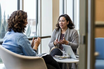 Two women engaged in a genuine and candid discussion about work in an office setting, reflecting authentic workplace interaction.

