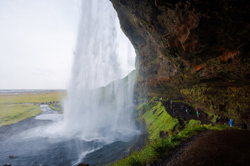 Fototapeta na wymiar Seljalandsfoss, a famous and unique waterfall in Iceland with visitors walking behind the falls into a small cave. Trip concept.