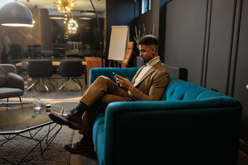 Modern office worker checking his smartphone while sitting on an office sofa