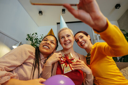 Three women taking a birthday selfie wearing birthday hats