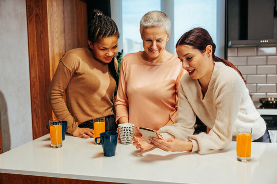 Three women in the kitchen watching something on the phone