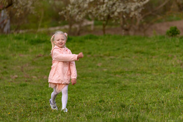 Portrait of little girl in pink outfit walking in green meadow. Child walks through clearing in spring park.