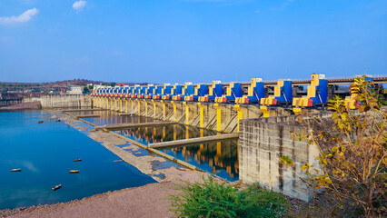 A beautiful view of the hydropower dam with a series of barrage gates looking toward a reservoir filled with blue water. The complete view amid a clear blue sky looks mesmerizing.