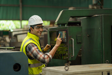 indian industrial worker beard man with helmet controlling cnc machine or maintenance in industry factory . labor male asian india Engineer standing repairing and fixing monitor in manufacturing.