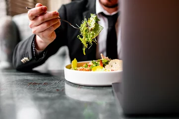 Tuinposter Busy at work. Businessman on business lunch at restaurant sitting at table eating vegetable salad  © pavel siamionov