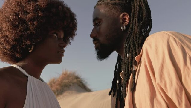 A black man and african woman stare deeply into each other's eyes, expressing affection and connection against an outdoor backdrop.
