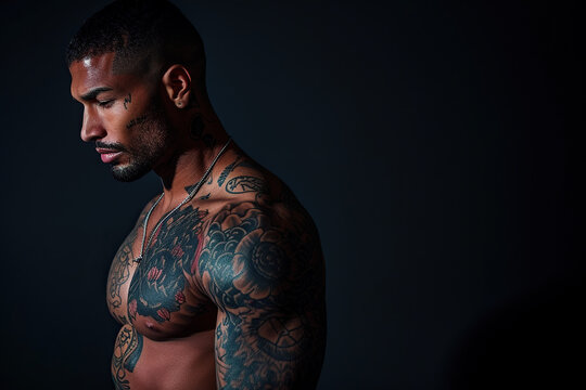 Confident African American man with muscular body tattooed on black background.