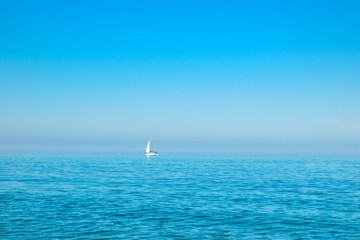 Obraz premium white sailboat on the open sea near the horizon against a cloudless sky. Boat trip. place for text